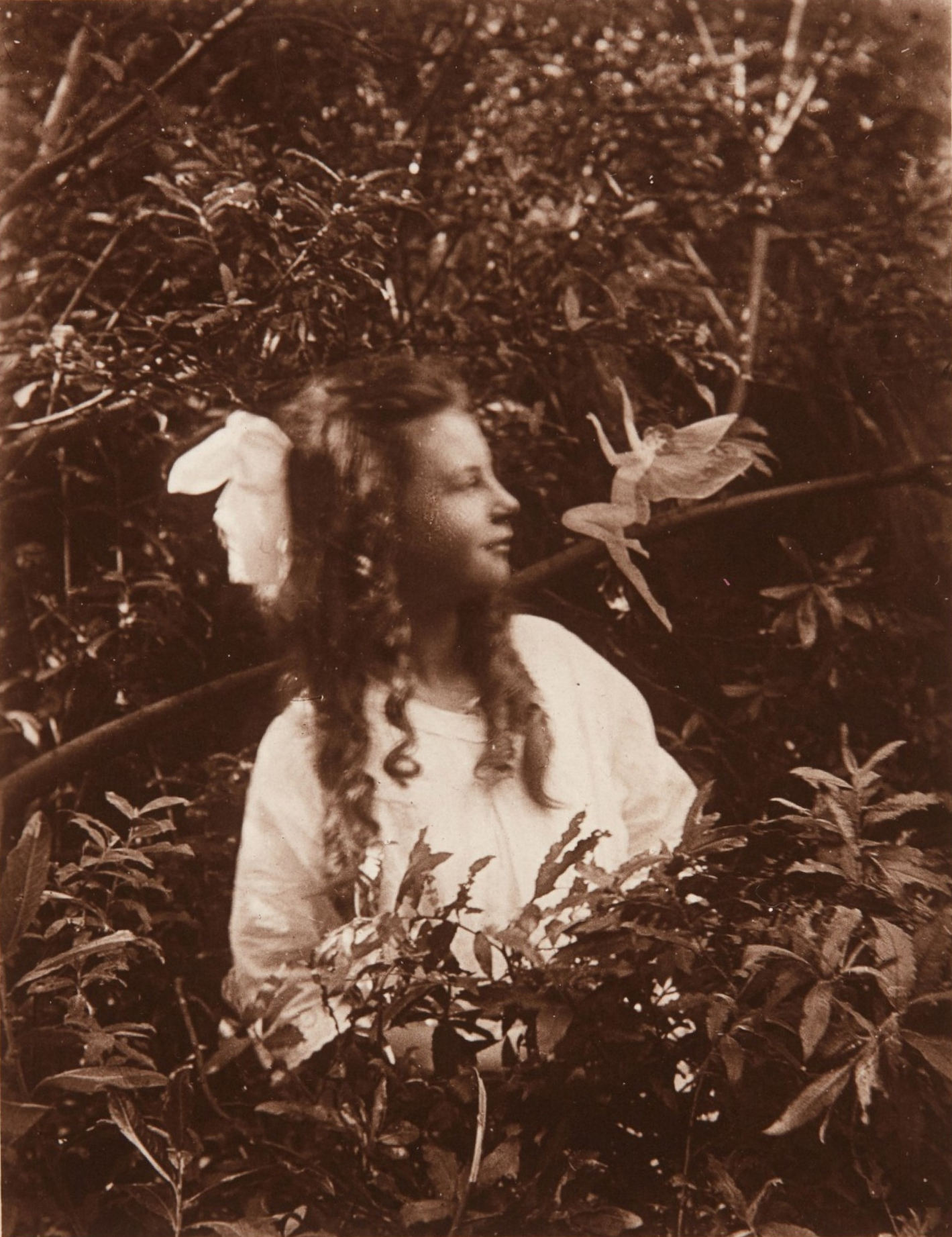 A young girl photographed outdoors with a small winged figure apparently standing in front of her