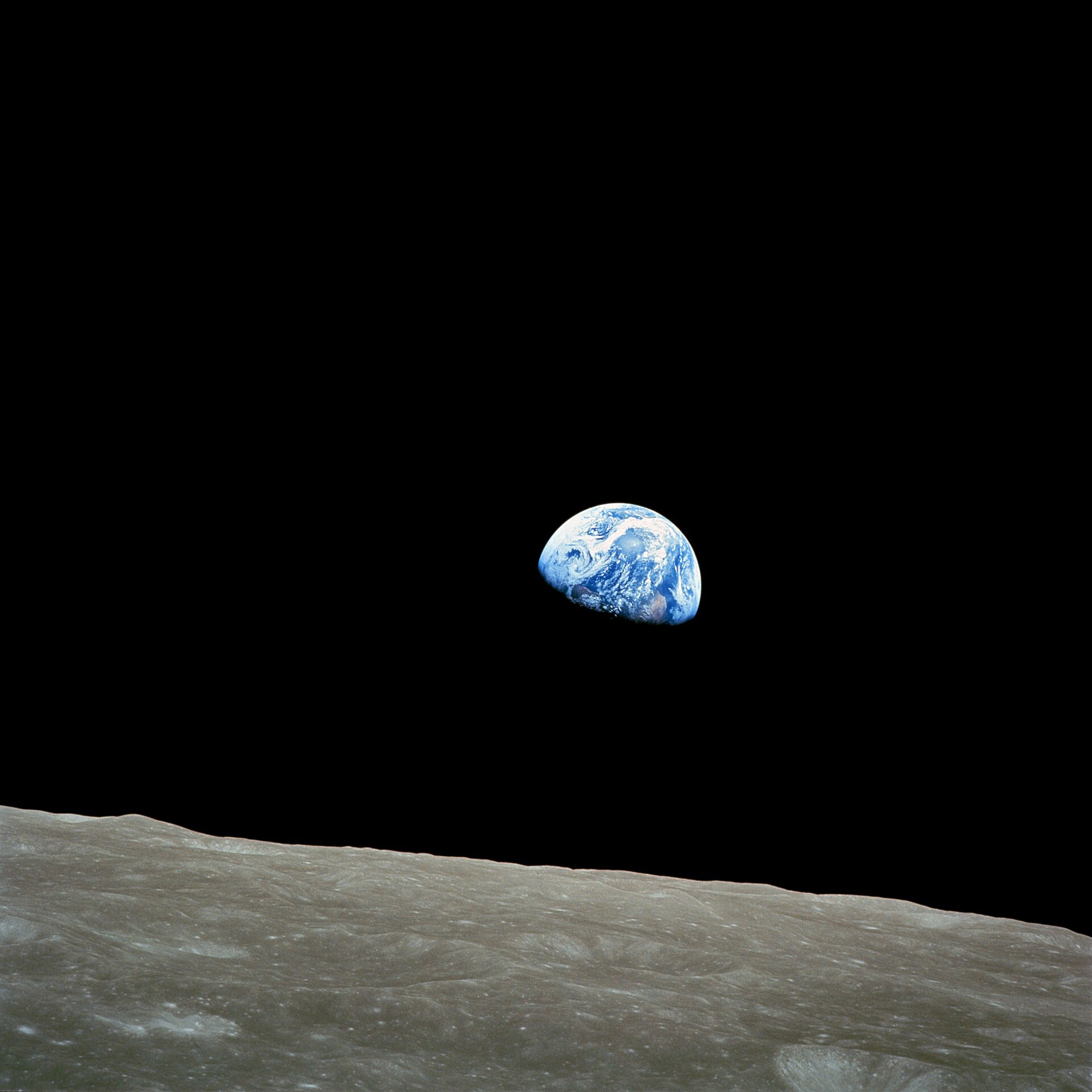 The Earth rising above the grey lunar horizon, photographed from lunar orbit