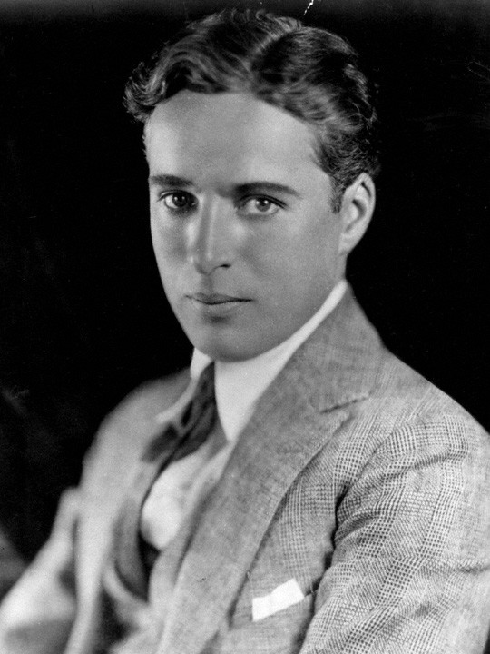 Studio portrait of Charlie Chaplin in a suit, looking directly at the camera