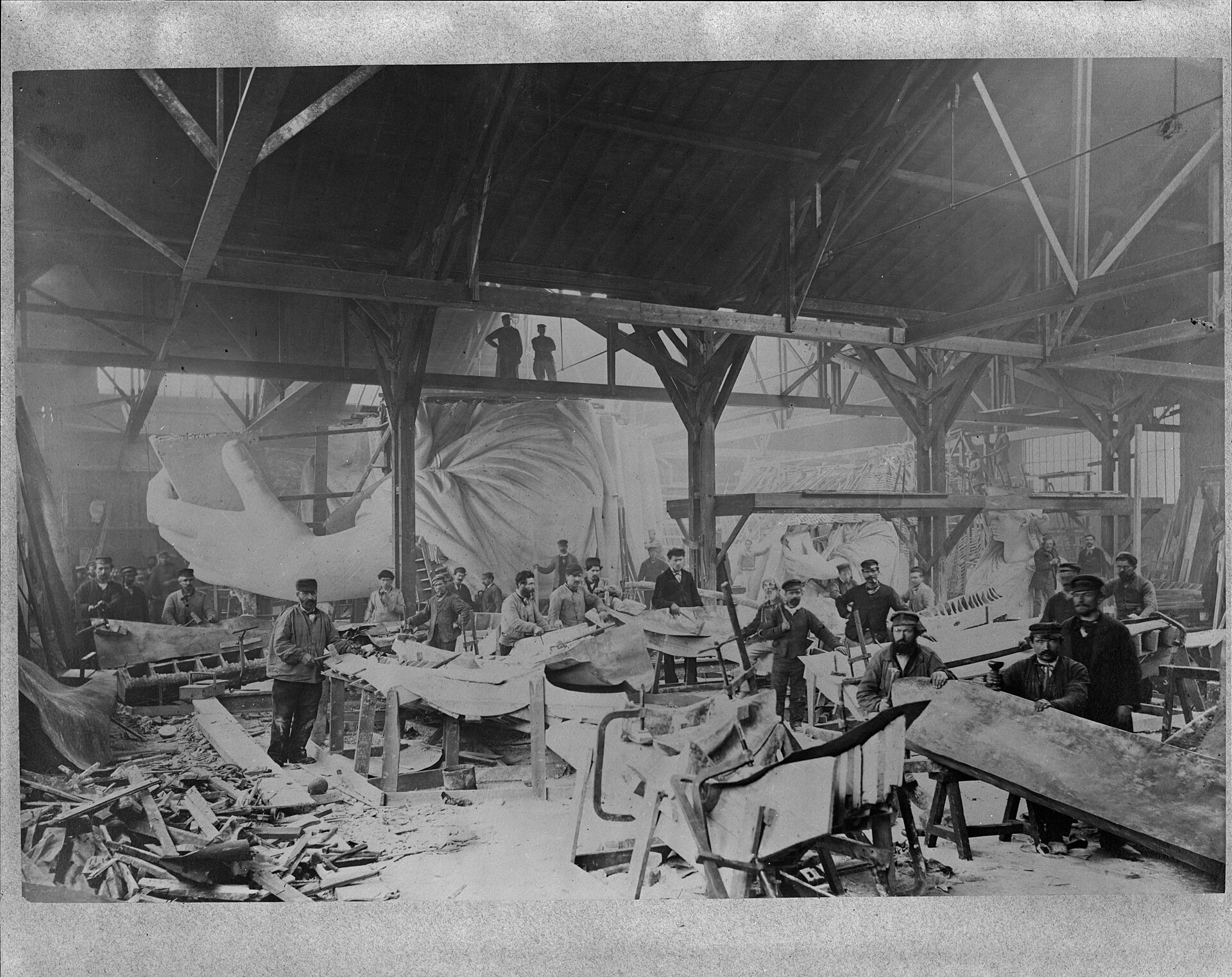 Workmen inside a Paris workshop beside the part-built left hand and quarter-size head of the Statue of Liberty