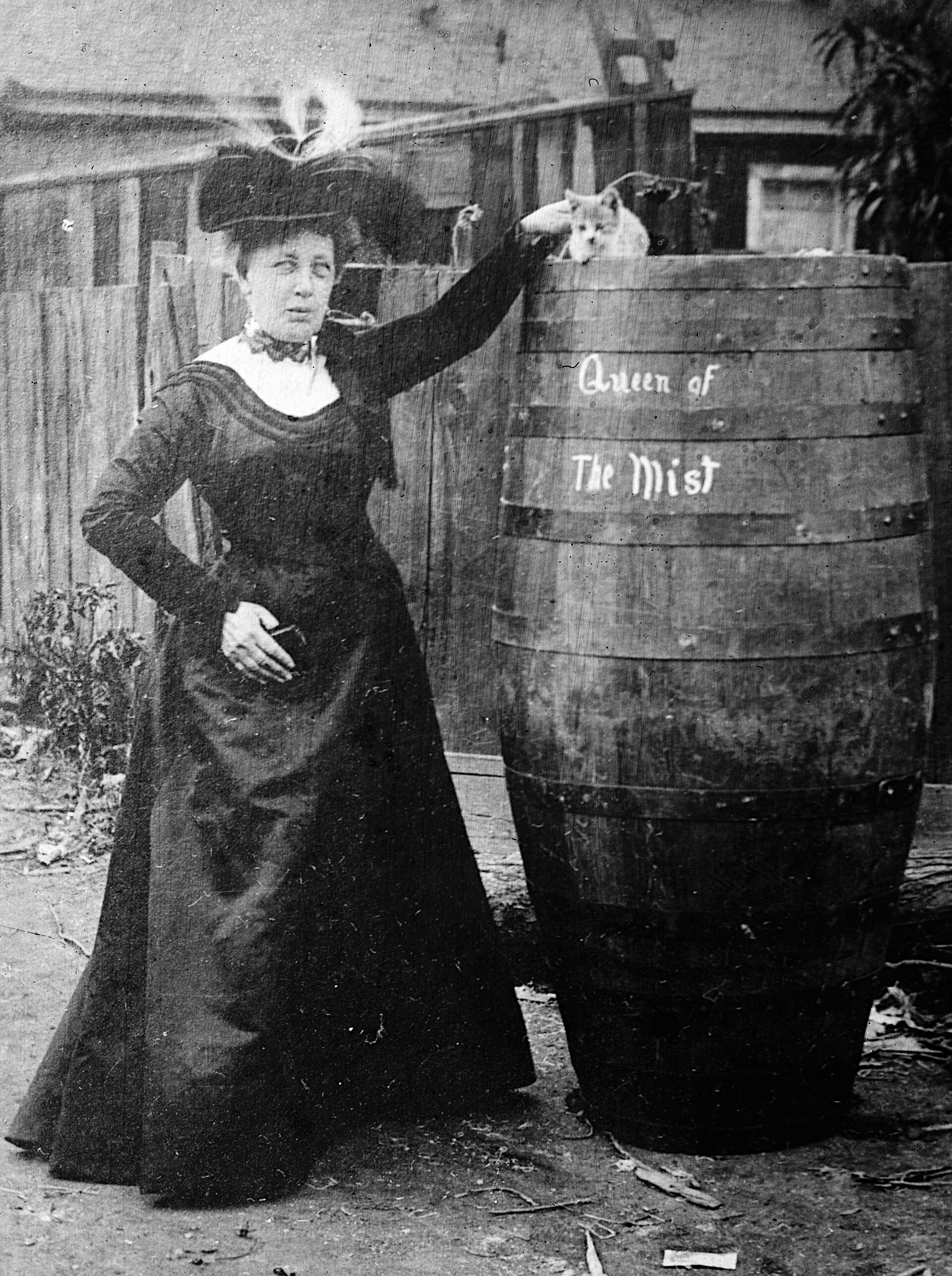 Annie Edson Taylor standing beside the wooden barrel she rode over Niagara Falls, with her cat