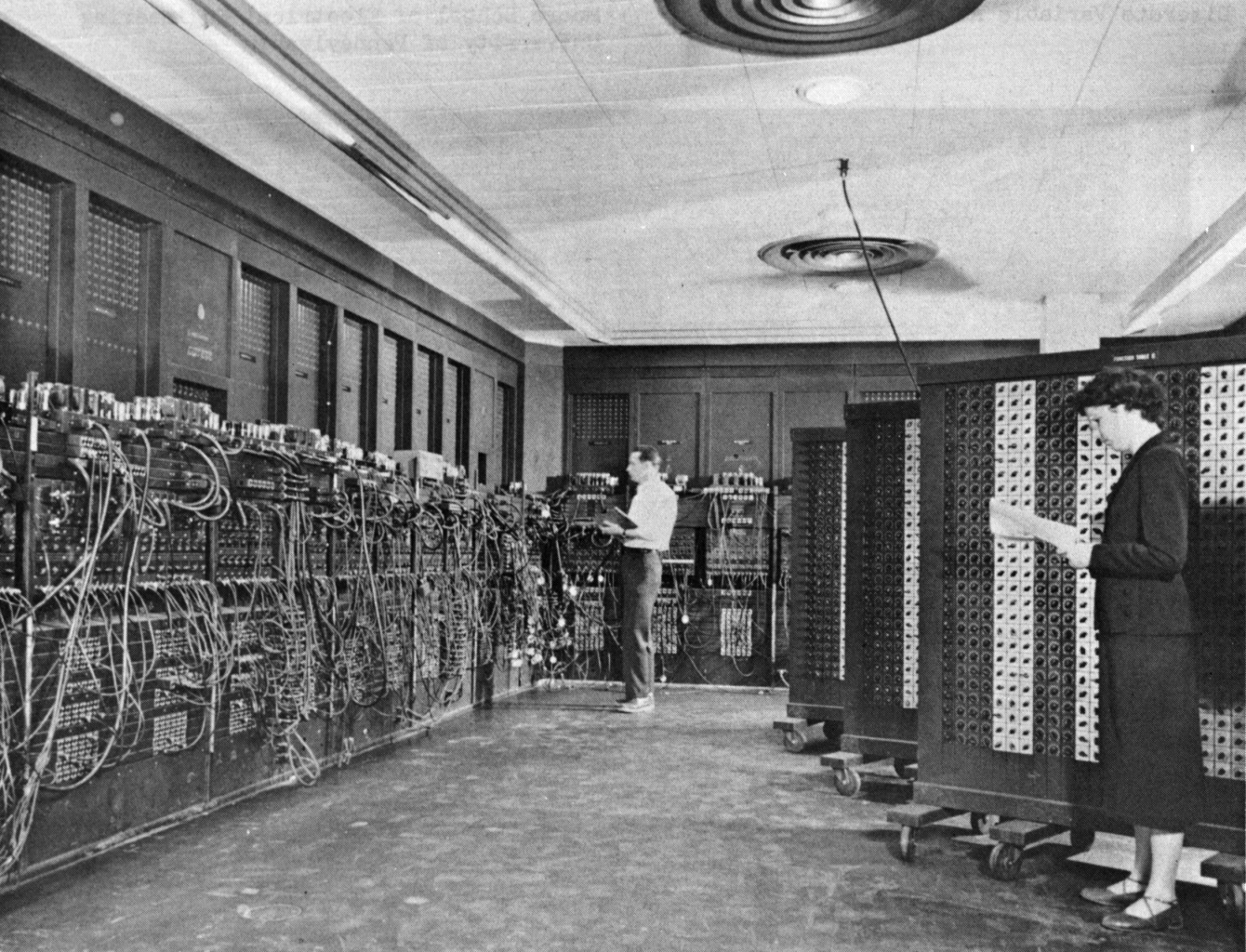 Two people setting switches and cables on the room-sized ENIAC computer