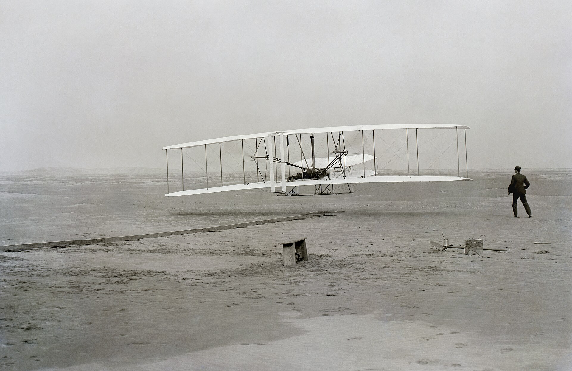 The Wright Flyer just off the ground at Kitty Hawk with Wilbur Wright running alongside the right wingtip